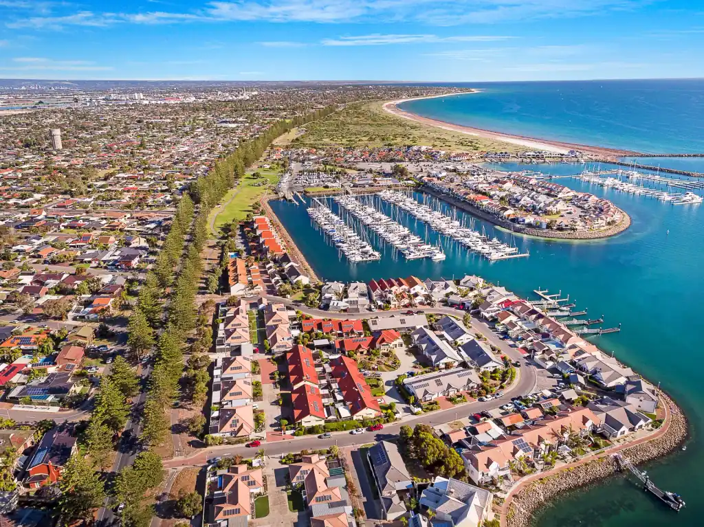 Aerial photograph of a coastal marina suburb at midday, houses and moored boats along the water, shot for a real estate listing