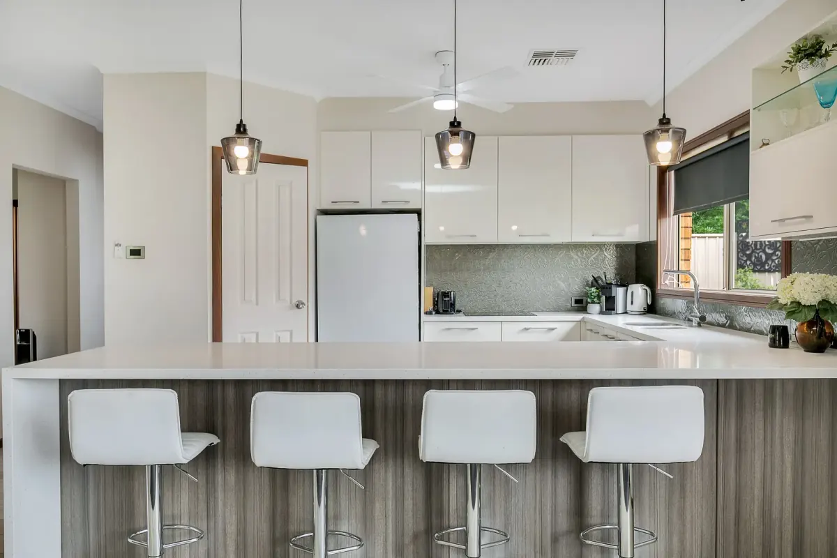 Real estate photo of a white kitchen with a long island bench and four stools, verticals straightened
