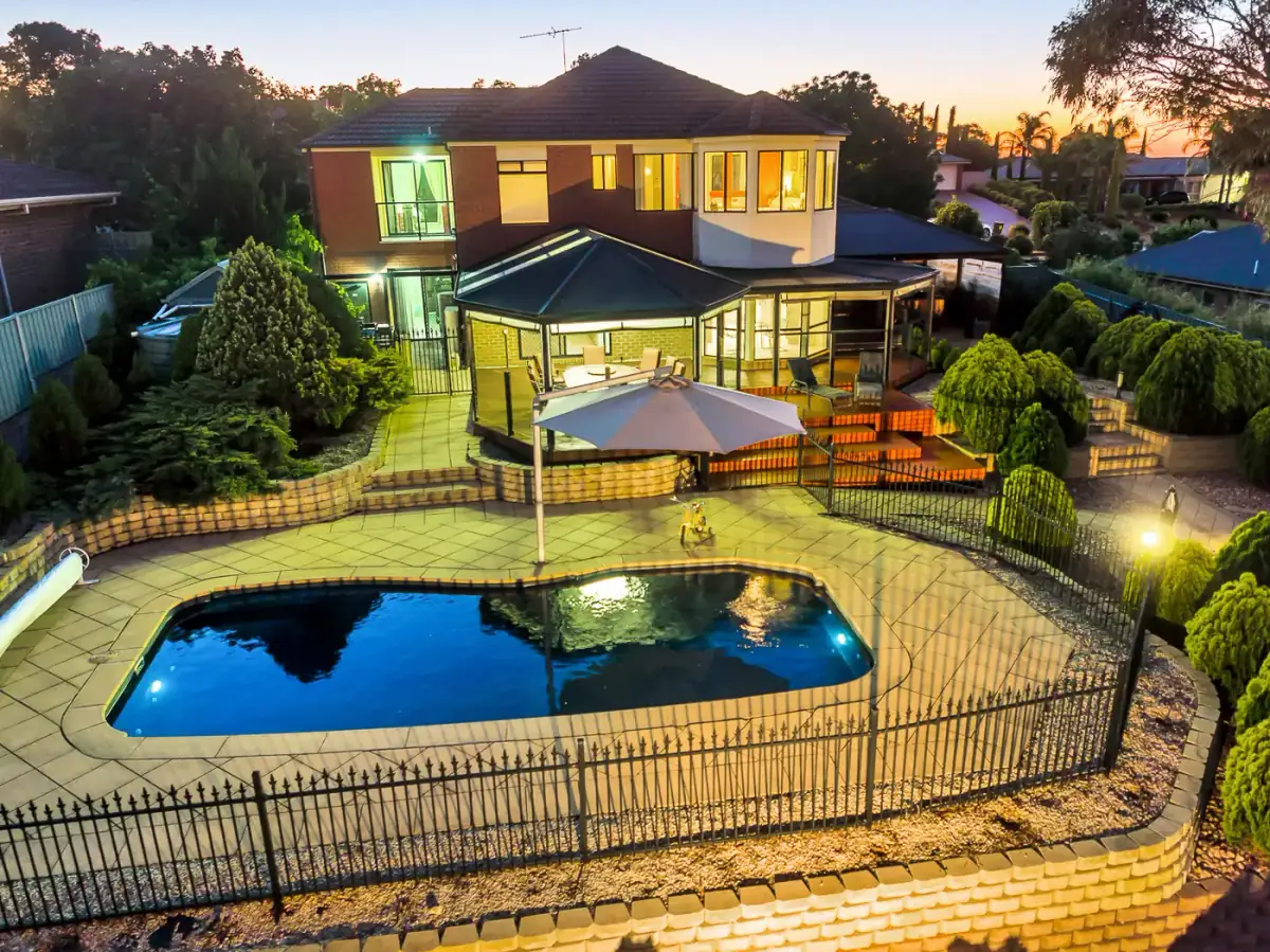 Twilight aerial real estate photo of a backyard pool with the house lights on